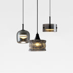 Three modern pendant lights with different glass shades—one rounded, one cylindrical, and one textured—hang from black cords against a plain white background. Two lights are turned on, emitting a warm glow.