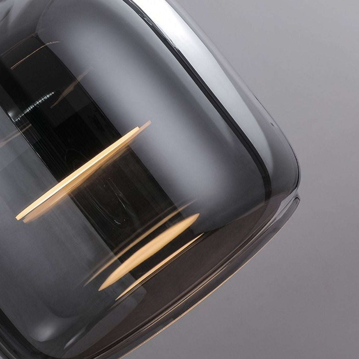 Close-up of a modern, glossy, dark gray pendant light glass lampshade with reflections of light strips on its smooth surface against a plain, light gray background.