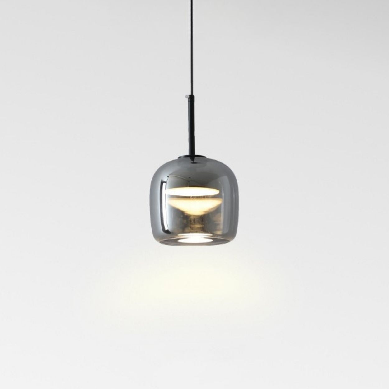 A modern pendant light with a glossy, rounded, transparent gray glass shade hangs from the ceiling, casting a soft glow on a plain white background.