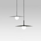 Two modern pendant lights hang from the ceiling, each featuring a flat, circular shade with a round white bulb beneath, set against a plain light gray background.