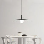 A modern dining area with a round white table, four white chairs, and black-and-white bowls. A black pendant light with a round bulb hangs above the table against a plain white wall.