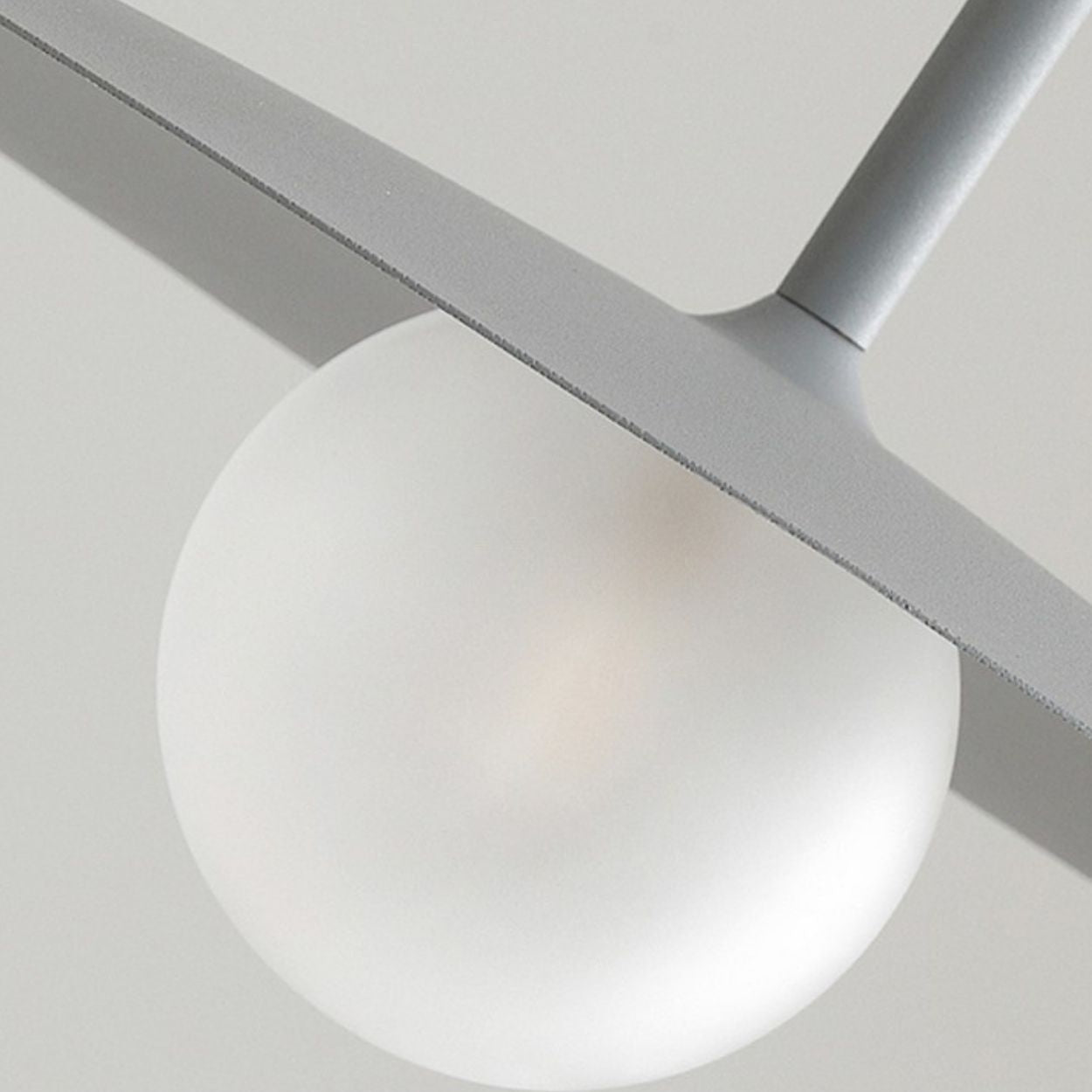 Close-up of a modern pendant light featuring a frosted glass globe partially covered by a flat, angled gray metal shade. The fixture is mounted on a gray metal rod against a neutral background.