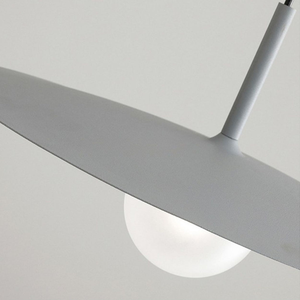 Close-up of a modern pendant light featuring a matte gray, disc-shaped shade and a round white bulb underneath, set against a plain light background.