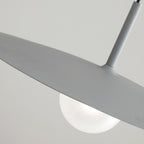 Close-up of a modern pendant light featuring a matte gray, disc-shaped shade and a round white bulb underneath, set against a plain light background.