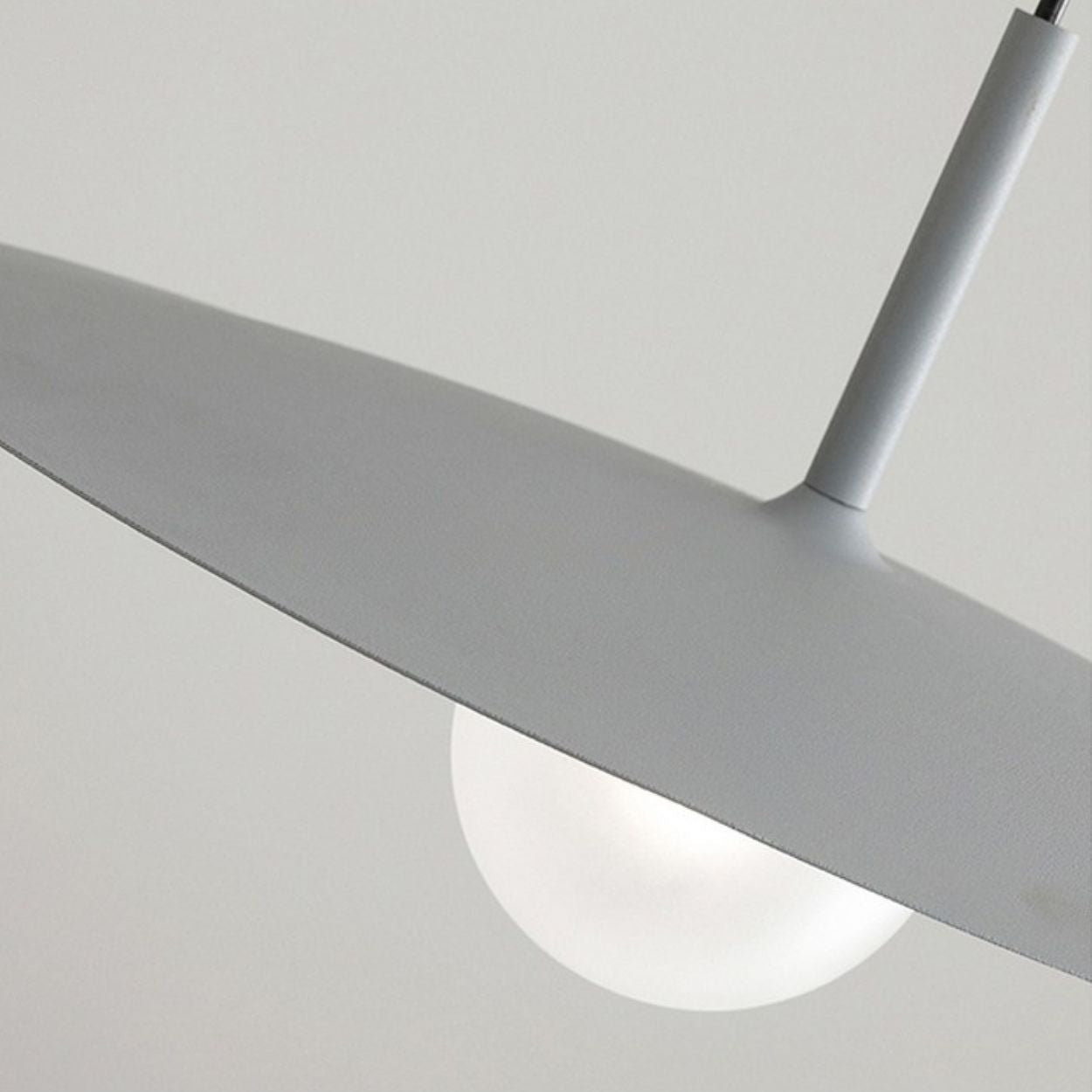Close-up of a modern pendant light featuring a matte gray, disc-shaped shade and a round white bulb underneath, set against a plain light background.