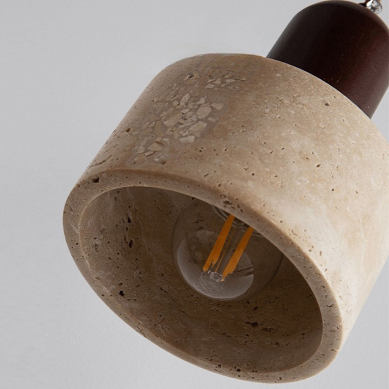 A close-up of a hanging pendant light fixture with a cylindrical, textured beige stone lampshade and an exposed bulb inside. The fixture is suspended from above against a plain light gray background.