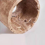 A close-up of a hanging pendant light fixture with a cylindrical, textured beige stone lampshade and an exposed bulb inside. The fixture is suspended from above against a plain light gray background.