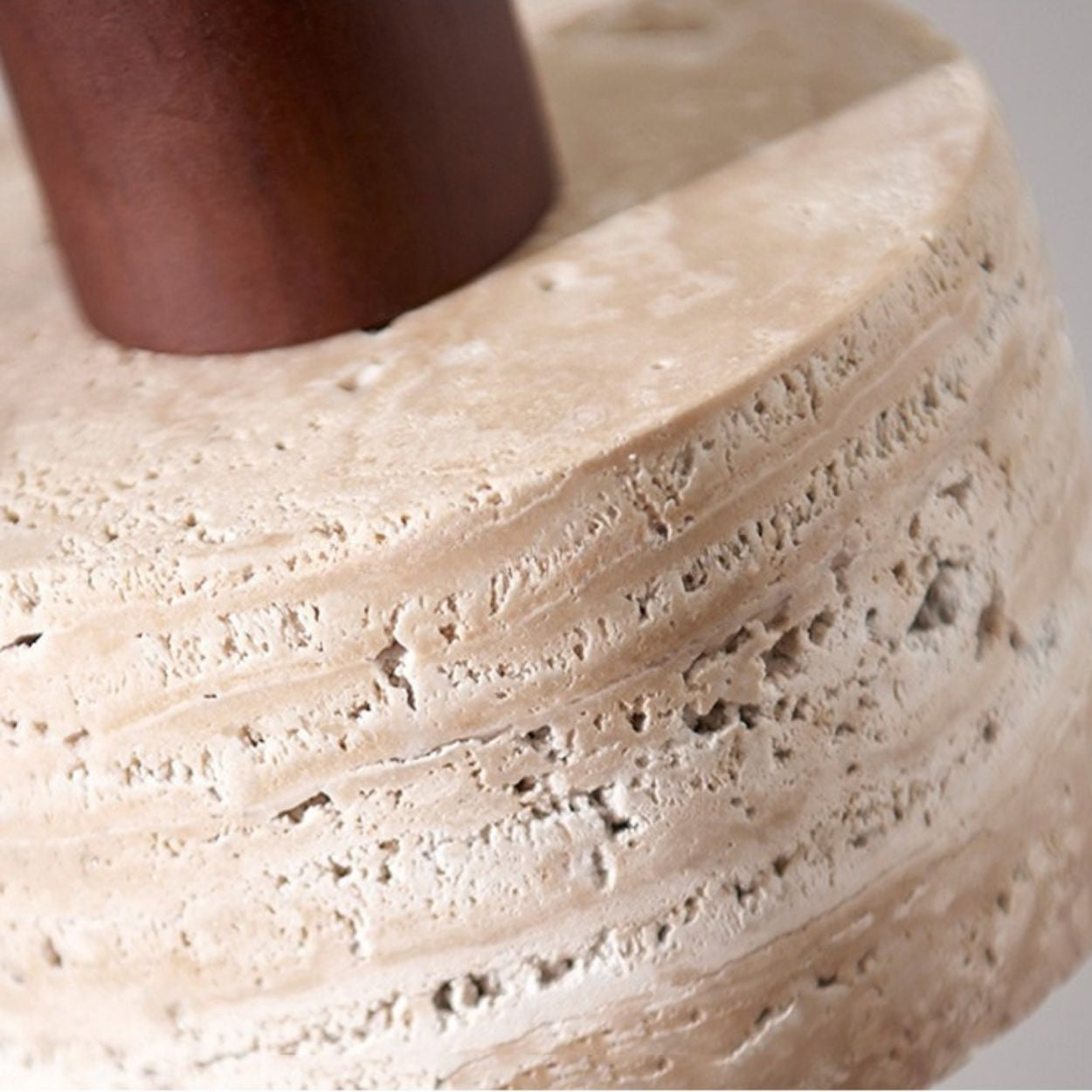 Close-up of a textured, beige stone with horizontal grooves, featuring a smooth, cylindrical brown rod inserted into it. The rough and porous surface adds character to this unique pendant light design.