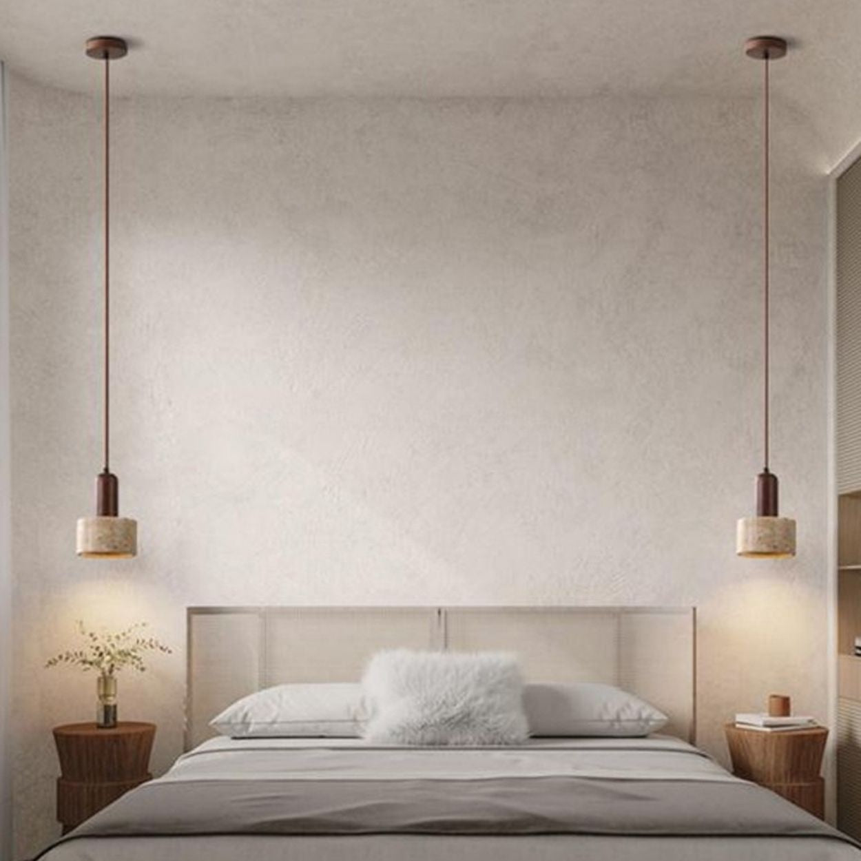 A minimalistic bedroom with a large bed, two pillows, and a fluffy white cushion. Pendant lights hang from the ceiling above wooden side tables, one topped with a vase of flowers. The neutral-toned walls and decor create a calm ambiance.