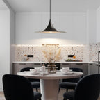 A modern kitchen with white cabinets and a terrazzo backsplash features a round dining table for four with black chairs. A striking pendant light hangs above the table, highlighting the dried flowers used as a centerpiece.