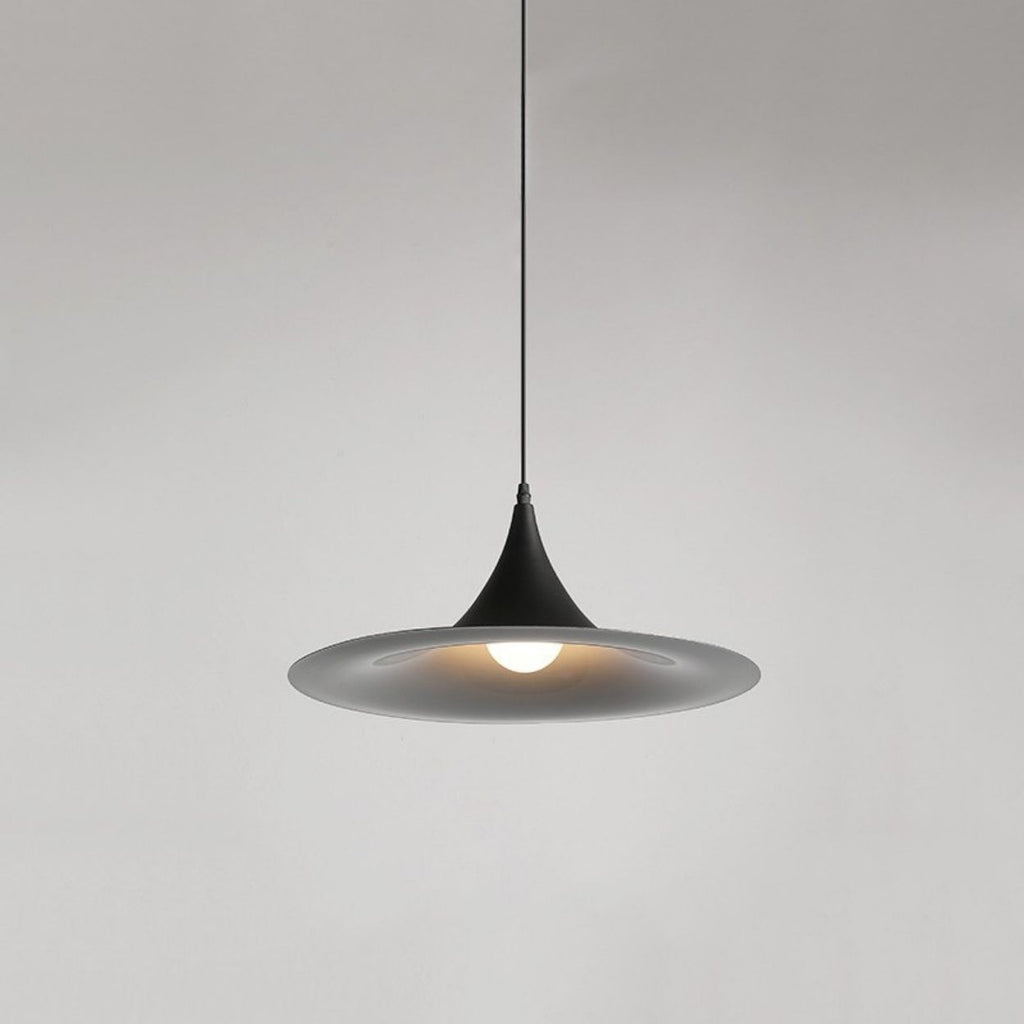 A modern, black pendant lamp with a wide, shallow shade hangs from the ceiling, emitting a soft light against a plain, light gray background.