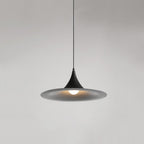 A modern, black pendant lamp with a wide, shallow shade hangs from the ceiling, emitting a soft light against a plain, light gray background.