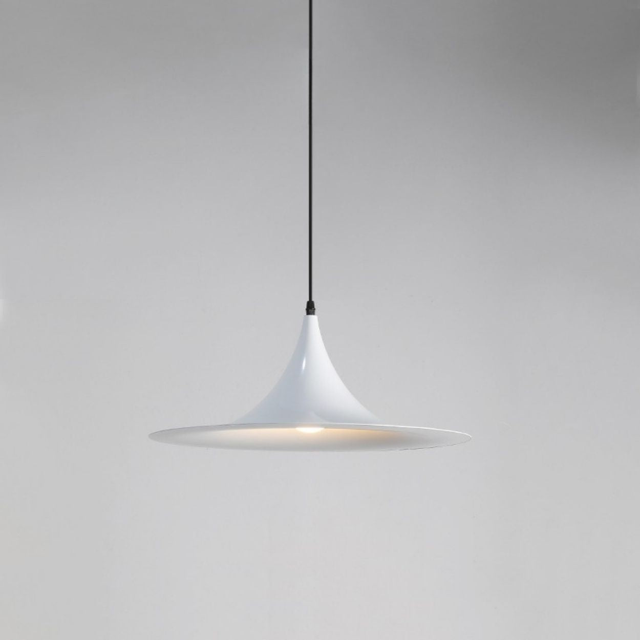 A modern, white pendant light with a sleek, cone-shaped shade hangs from a thin black cord against a plain gray background.