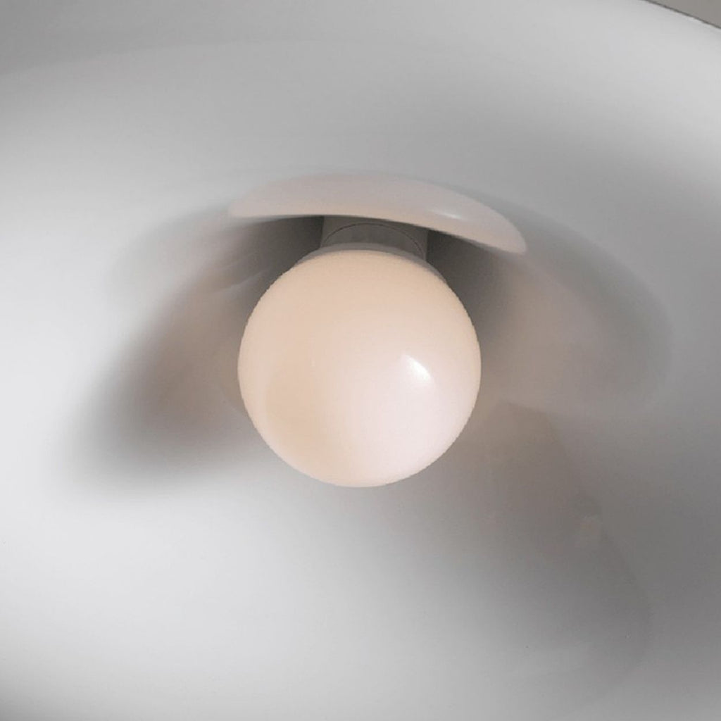A close-up view of a round white light bulb mounted inside a smooth, white pendant light lampshade, seen from directly below.