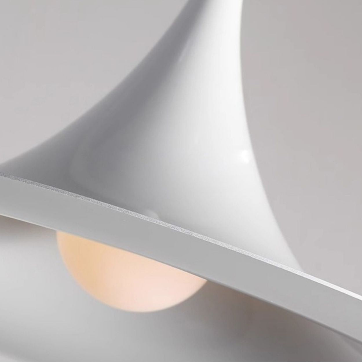 Close-up of a modern white pendant light with a smooth, curved design. A soft glowing bulb is partially visible beneath the stylish pendant light, creating gentle illumination against a neutral, minimalistic background.