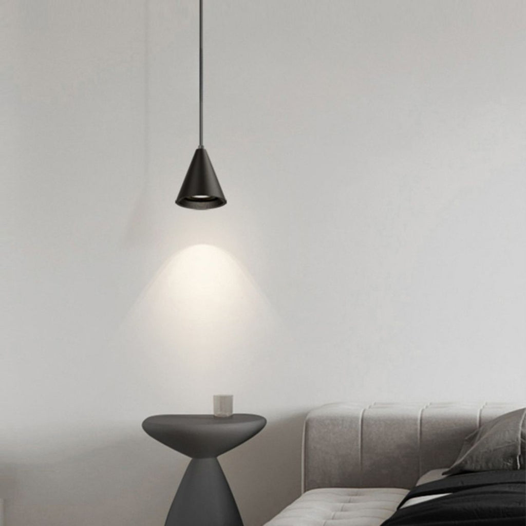 A modern, minimal bedroom with a gray upholstered bed, a small round side table, and a cone-shaped black pendant light casting light on the wall, creating a cozy and simple atmosphere.