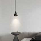 A modern, minimal bedroom with a gray upholstered bed, a small round side table, and a cone-shaped black pendant light casting light on the wall, creating a cozy and simple atmosphere.