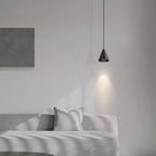 A minimal living room with a light gray sofa, a matching pillow, a blank rectangular wall art, and a single black pendant lamp casting light on the wall above. The scene is calm and uncluttered.