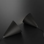 Two black, cone-shaped pendant lights lie on a dark surface, facing each other with light subtly shining from one toward the other. Both lamps have cords extending from their bases.