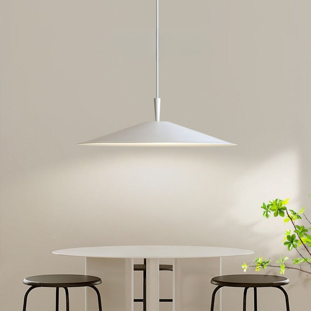 Minimalist dining area with a white round table, two black stools, a modern white pendant light above, and a small green plant in the corner against a neutral beige wall.