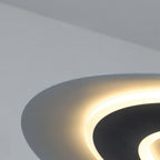 A close-up of a modern, circular pendant light fixture with a glowing halo effect, mounted on a white ceiling. The fixture emits soft, warm light and features a sleek, curved design.