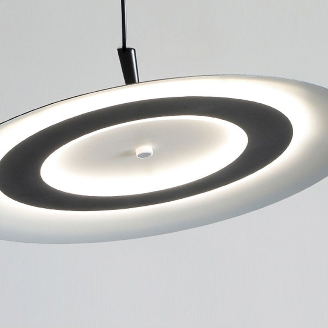 A modern, circular pendant ceiling light with a glowing ring design, this elegant pendant light emits soft white light and is suspended by a black cord against a plain light background.
