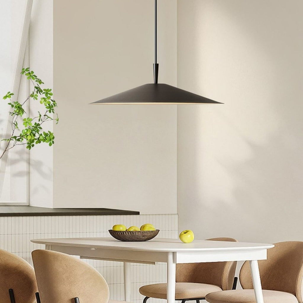 A modern dining room with a white table, beige chairs, and a striking pendant light hanging above. A bowl of green apples sits atop the table, while a plant on the windowsill enhances the minimalist, neutral design.