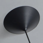A close-up view of a black, cone-shaped pendant light mount lampshade on a light-colored wall, with a cord extending from the narrow end.
