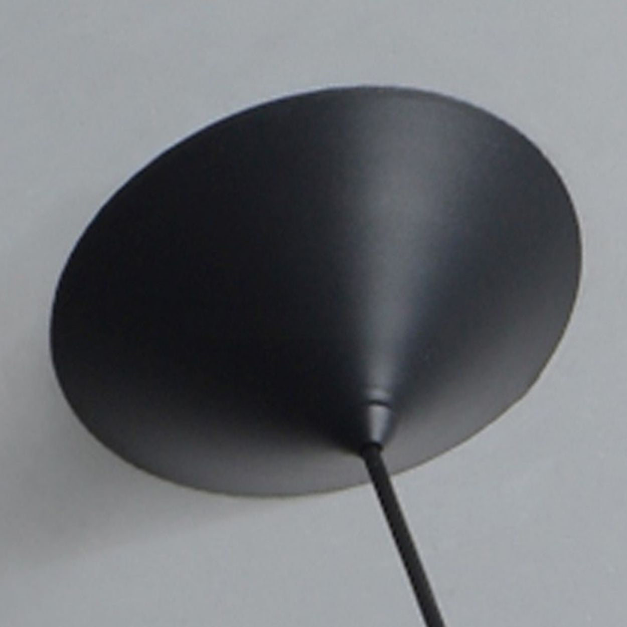 A close-up view of a black, cone-shaped pendant light mount lampshade on a light-colored wall, with a cord extending from the narrow end.