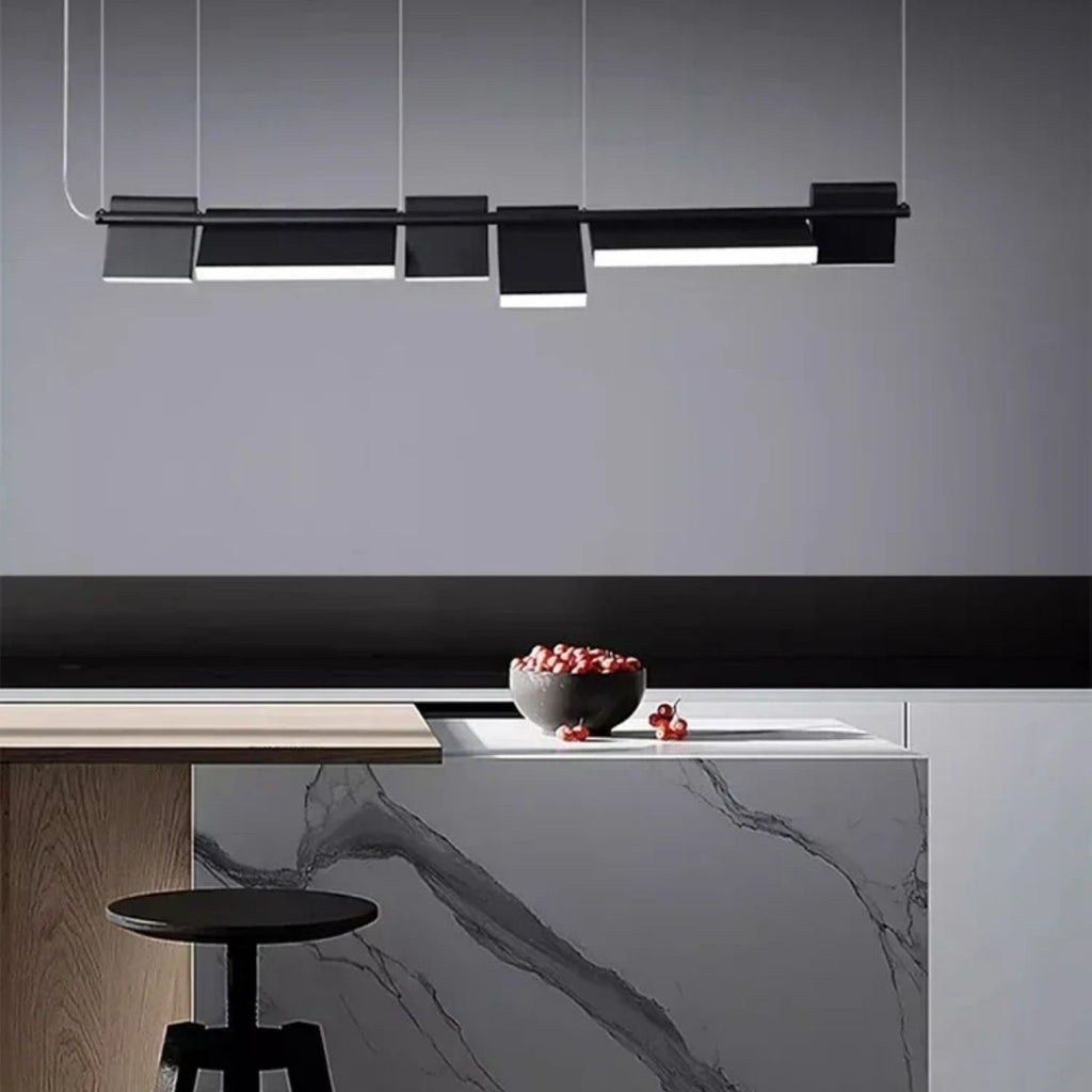A modern kitchen featuring a marble-patterned island, a black stool, a bowl of cherries, and a sleek pendant light illuminating the counter against a gray wall.
