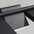 Close-up of a modern, black metal pendant light with a sleek, angular design and smooth surface, mounted on a light-colored wall or ceiling.