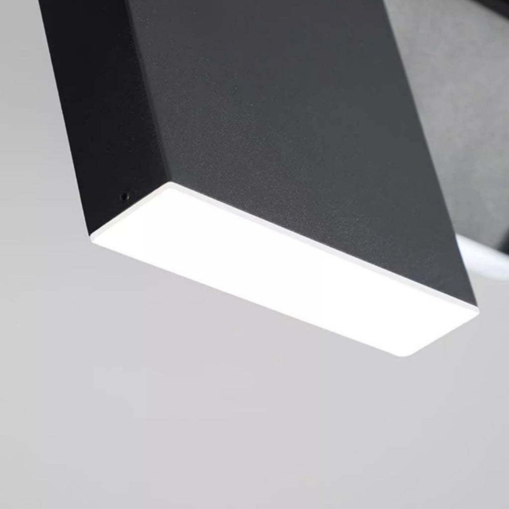 A close-up view of a modern, rectangular black pendant light fixture with a bright illuminated surface against a plain light gray background.