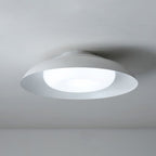 A modern, circular ceiling light fixture in white is mounted on a plain white ceiling, emitting a soft, diffused glow.