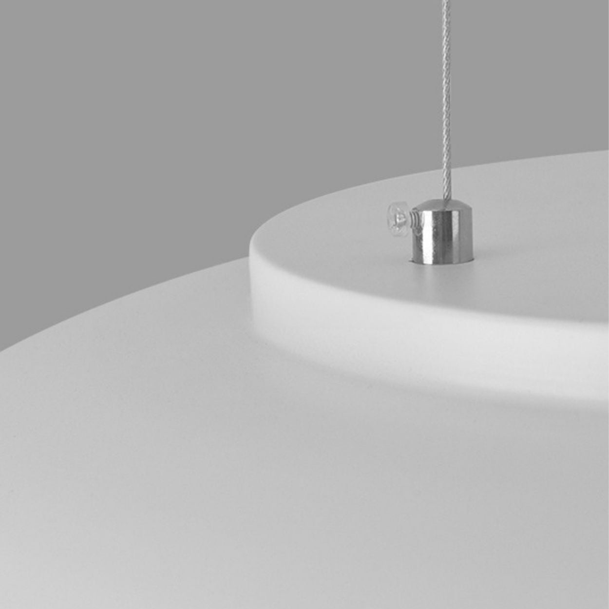 Close-up of a modern white pendant light fixture with a silver metal attachment and a thin suspension cable against a plain grey background, highlighting the ceiling light close up in detail.