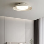 A modern ceiling light fixture emits a soft glow in a minimalist bedroom with light gray walls, a bed below, sheer curtains, and dark drapes by the window.