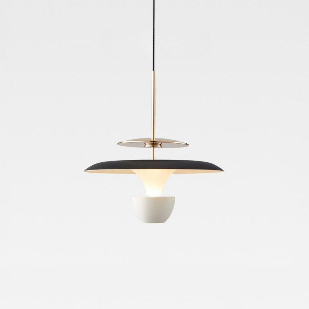 A modern pendant light with a black and gold circular shade, suspended by a thin black cord, features a white bowl-shaped diffuser beneath it, creating a striking look against the plain light gray background.