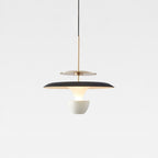 A modern pendant light with a black and gold circular shade, suspended by a thin black cord, features a white bowl-shaped diffuser beneath it, creating a striking look against the plain light gray background.