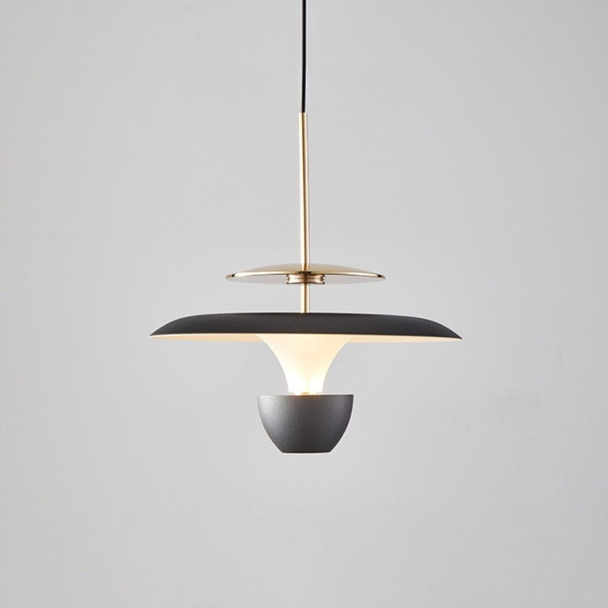 A modern luxury pendant light fixture with a black and gold finish, featuring a wide, flat shade and suspended from a black cord against a plain light gray background.