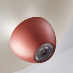 A close-up of a modern, dome-shaped red pendant light with a textured surface, mounted on a smooth off-white ceiling. The luxury fixture’s lens and bulb are visible at the center.