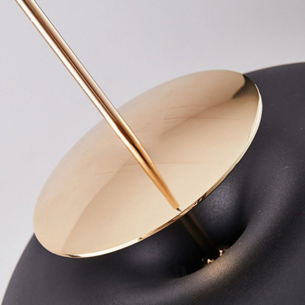 A closeup of a luxury modern lamp with a black rounded base and a gold circular disk intersected by a gold rod, creating a minimalist and elegant design.