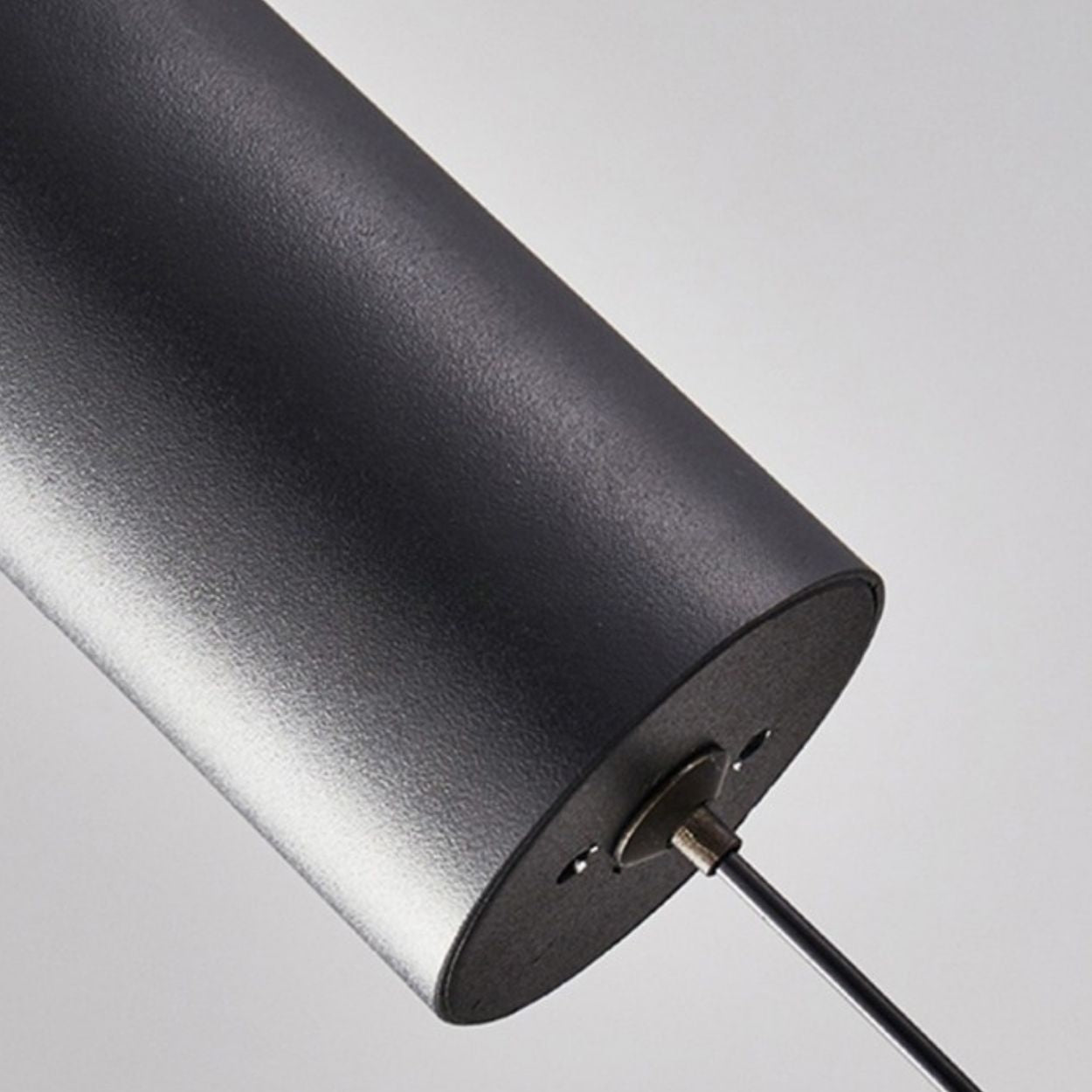 Close-up view of a cylindrical, matte black metallic pendant light with a wire protruding from one flat end, set against a plain, light gray background.