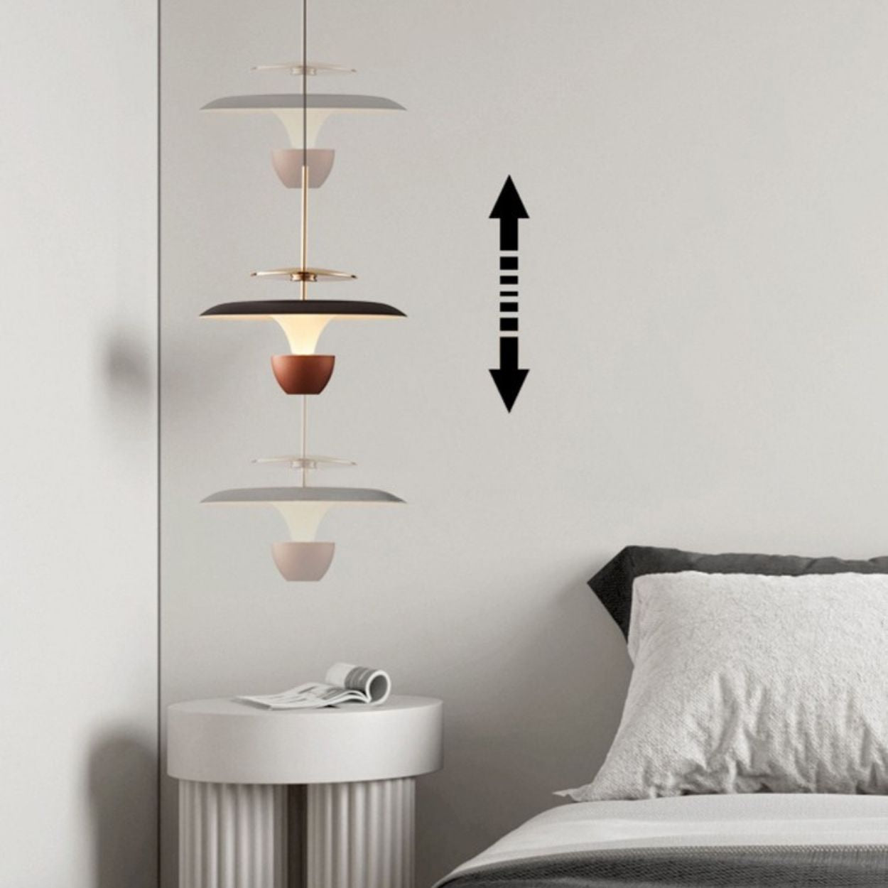 A modern luxury pendant light with layered, cone-shaped shades hangs above a white round side table next to a bed. A double-headed vertical arrow on the wall indicates the lamp’s adjustable height.