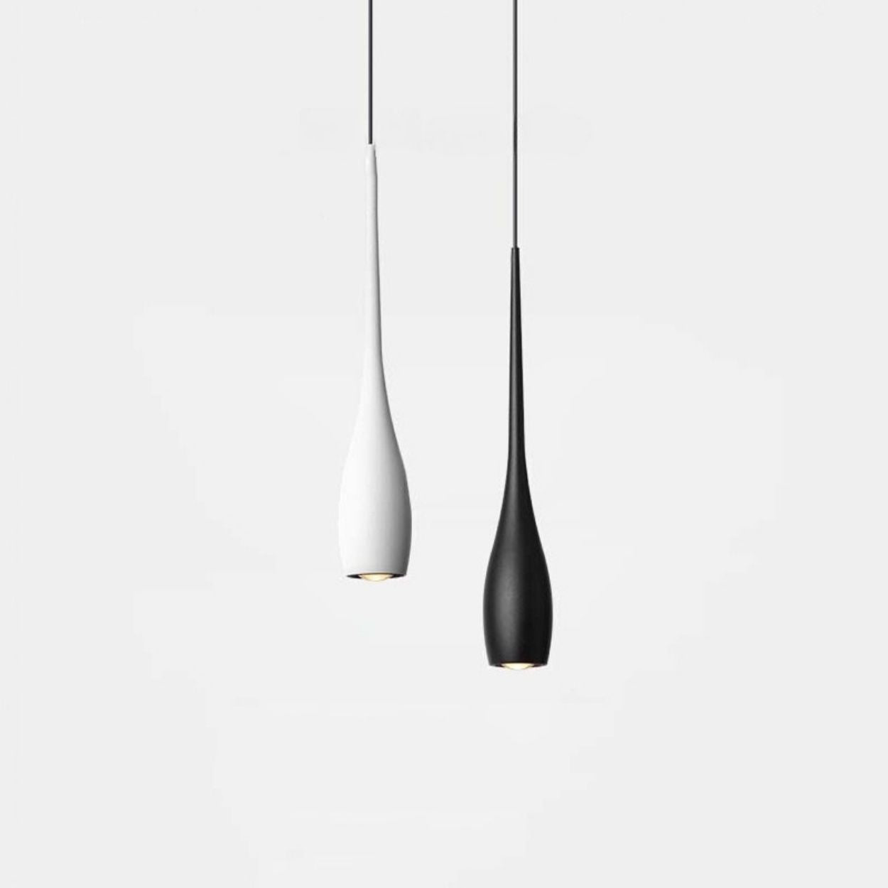Two modern pendant lights with slim, elongated shapes hang side by side against a plain white background; one pendant light is white and the other is black.