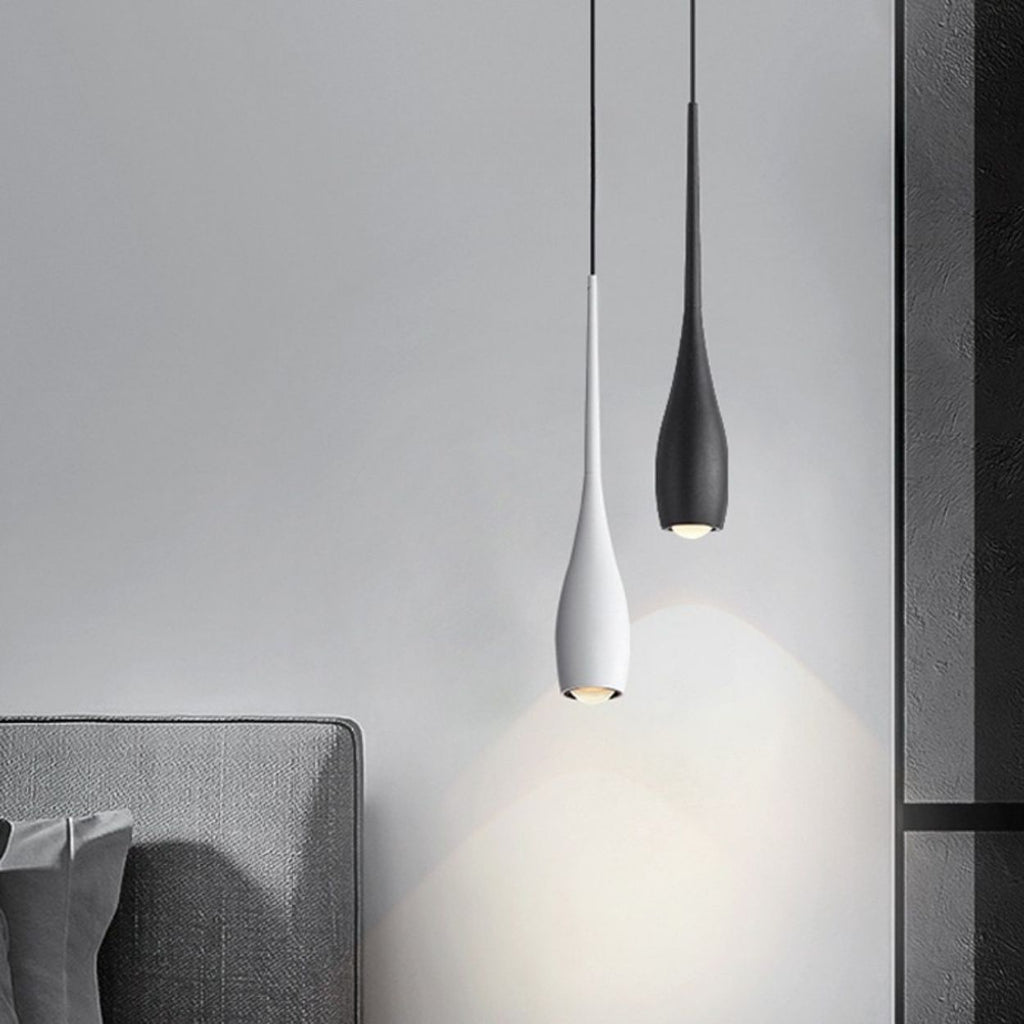 Two modern pendant lights, one white and one black, hang above a gray upholstered bed and cast soft light on a light gray wall in this minimalist bedroom setting.