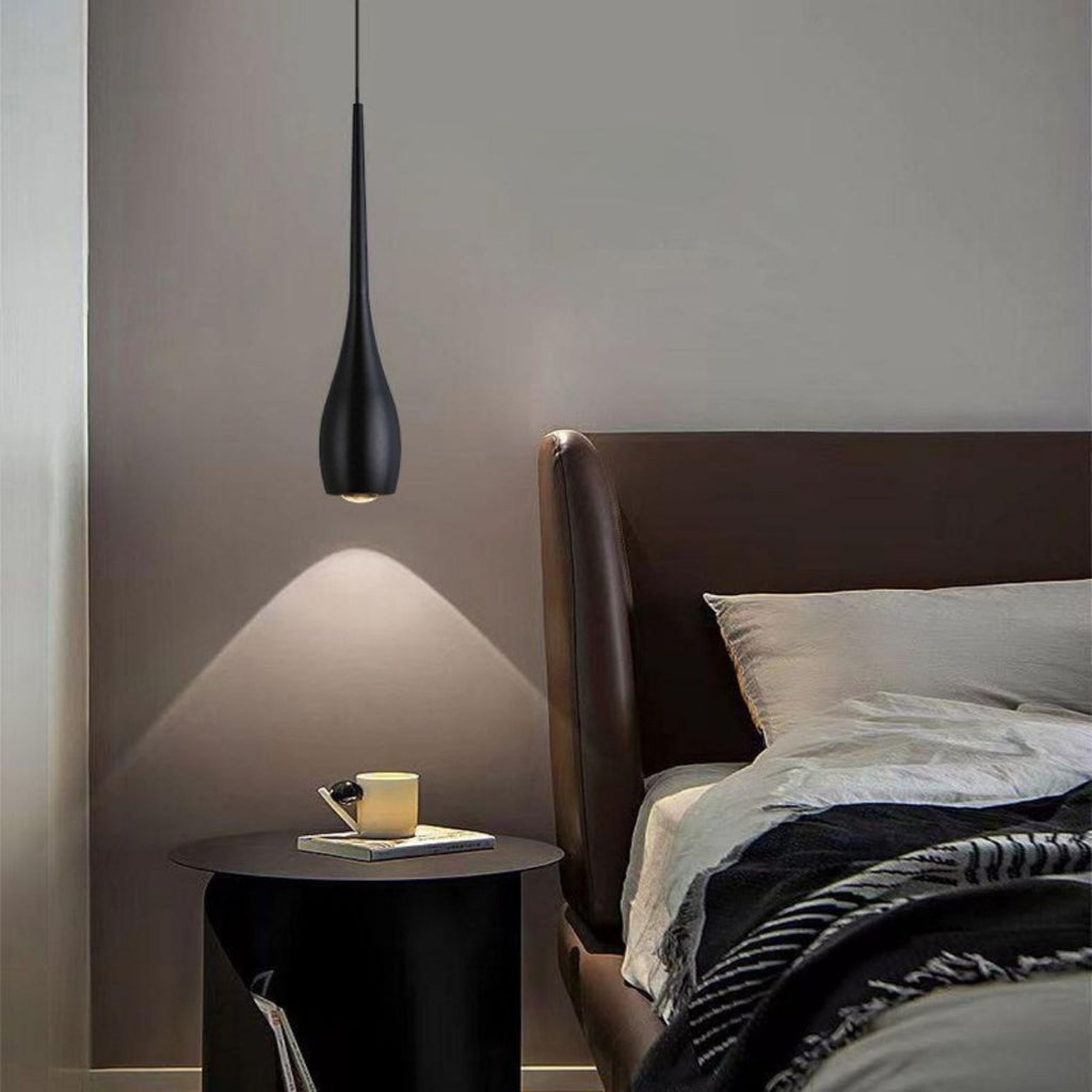 A modern bedroom with a dark brown upholstered bed, white and gray bedding, and a round bedside table holding a smartphone, pen, and glass of water, all illuminated by a stylish pendant light against a gray wall.