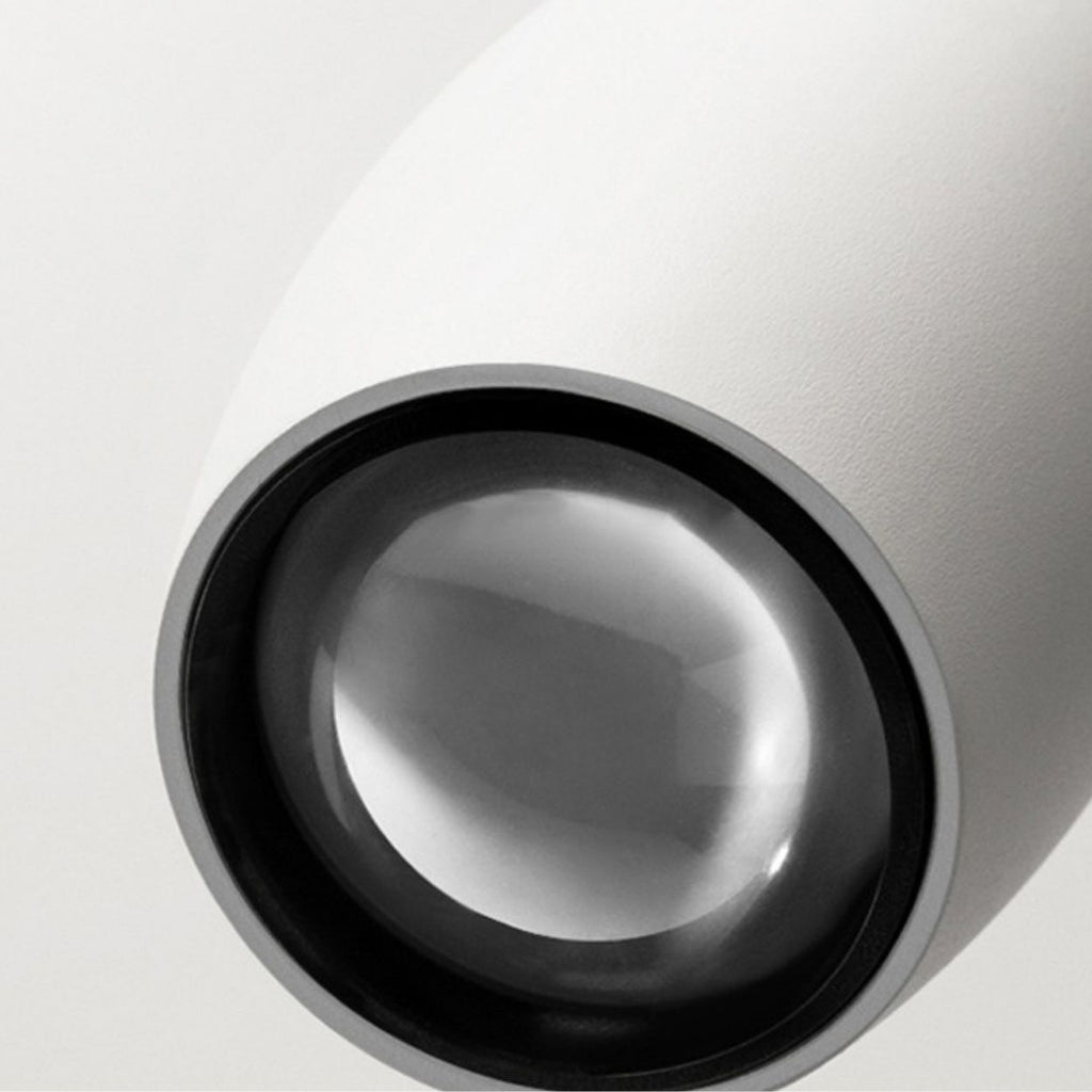 Close-up of a modern, minimalistic white pendant light with a round, reflective glass lens or surface, featuring a smooth texture and clean lines against a light gray background.