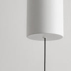 Close-up of a modern, cylindrical white pendant light mount hanging from a thin black cord against a plain light gray wall.