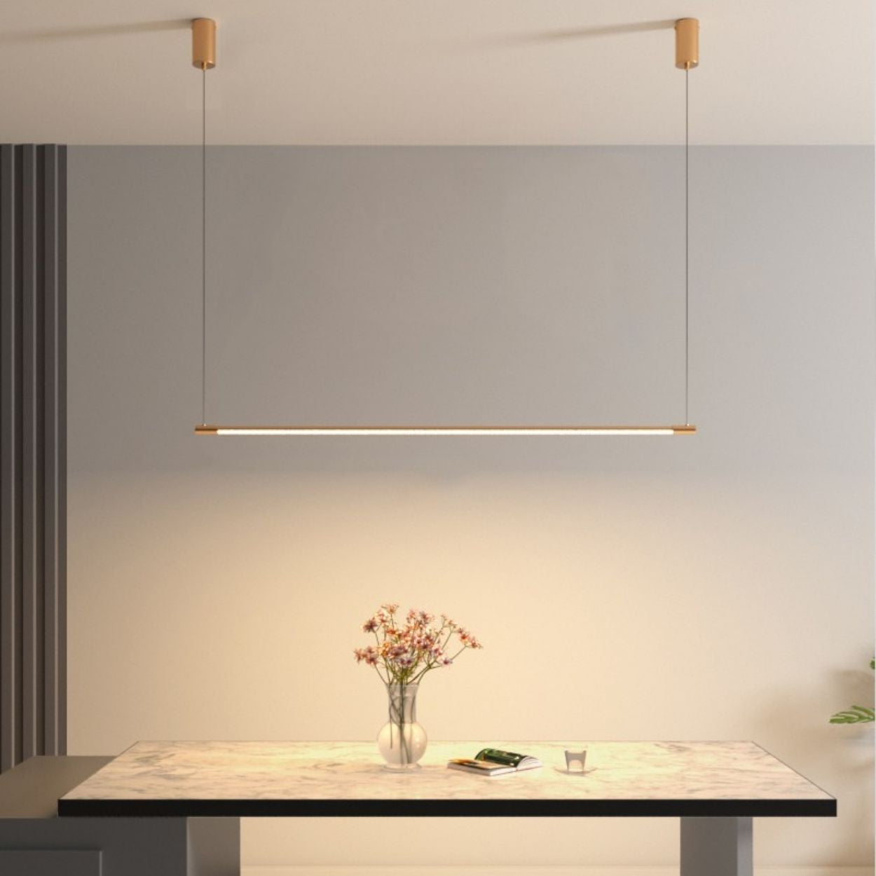 A minimalistic dining area features a rectangular marble table, a small vase of flowers, and a sleek pendant light suspended above, all set against a neutral wall with vertical paneling.