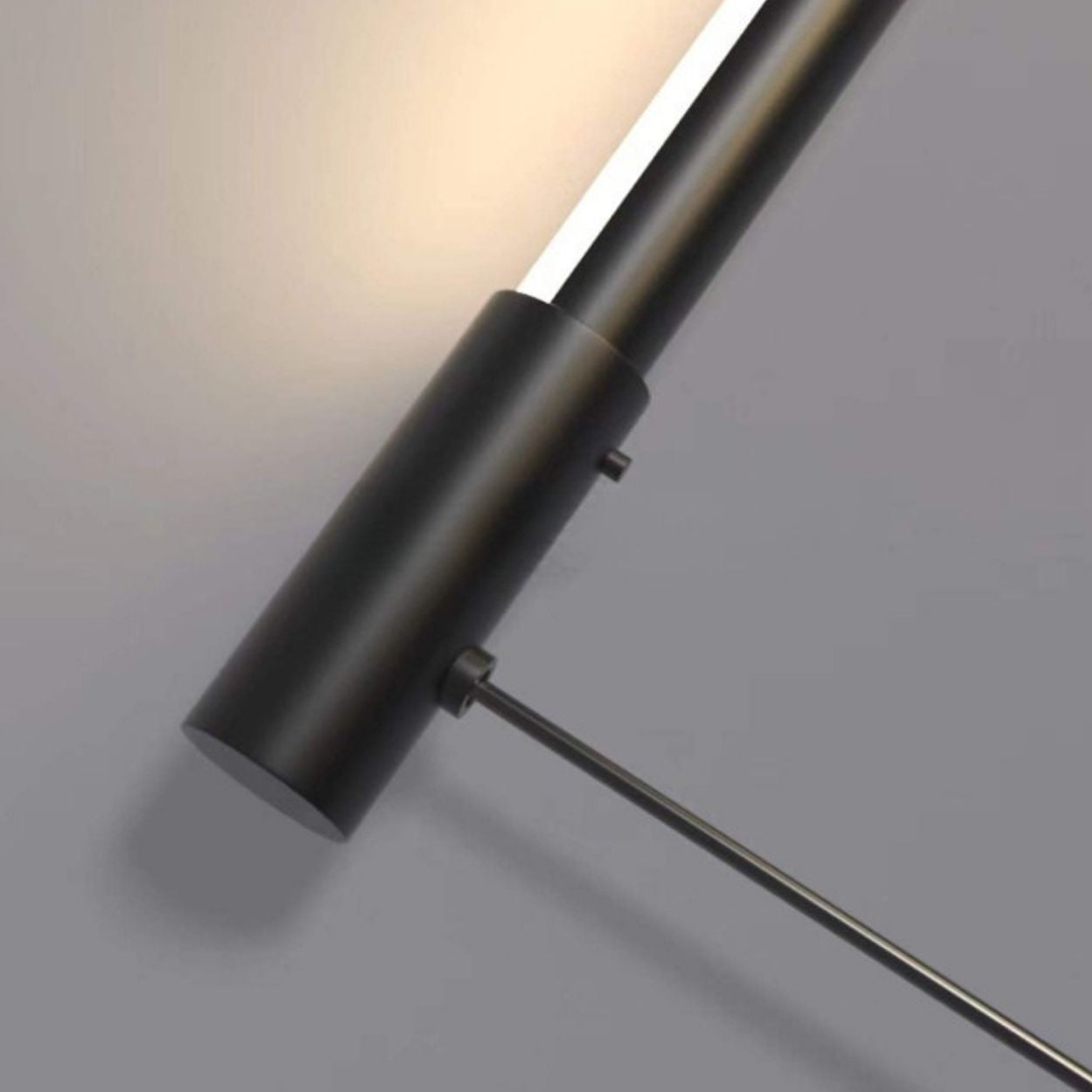 A close-up of a modern, cylindrical black wall-mounted light fixture on a gray wall, emitting a warm glow upward, reminiscent of a Pendant Light Close Up.