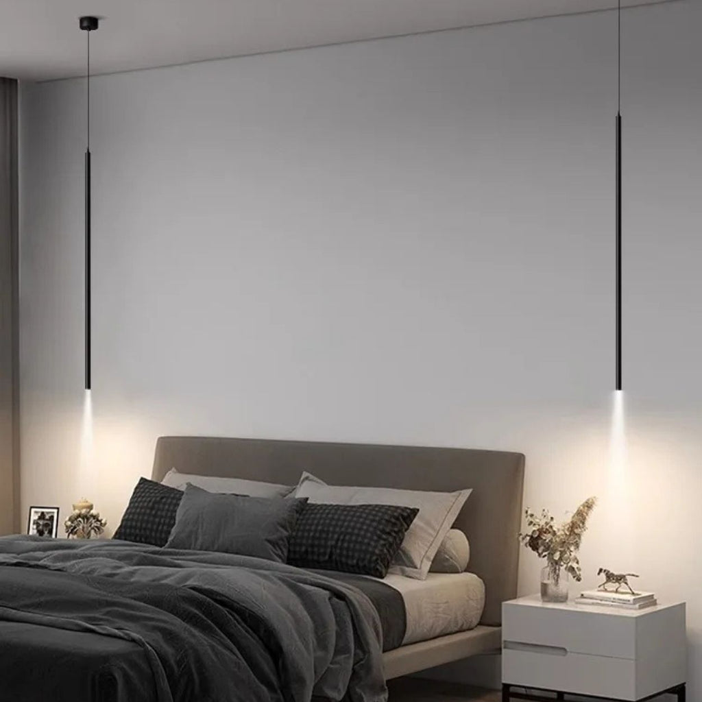 A modern minimalist bedroom with a gray bed, dark and light bedding, two white nightstands, decorative items, and slim pendant lights hanging from the ceiling, casting a soft pendant light downward.